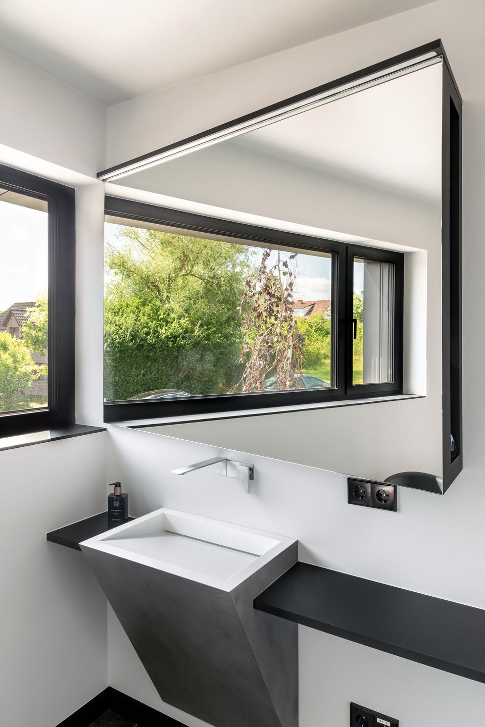 Waschplatz mit wandhaengendem Becken und grossem Fenster Waschplatz mit trapezfoermigem wandhaengendem Waschbecken, wandmontierter Armatur, grossem Spiegel und Fenster mit schwarzem Rahmen