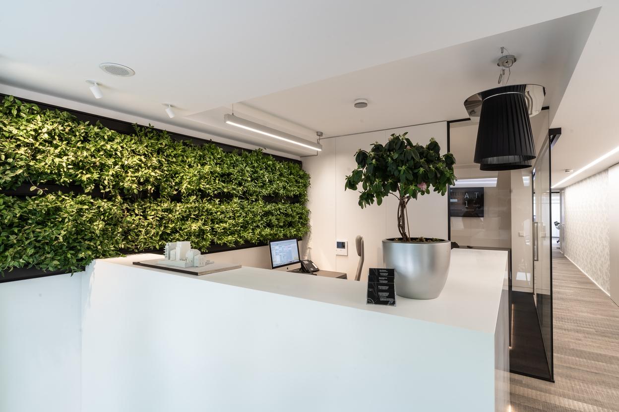 Accueil avec poste informatique, grand comptoir blanc, plante en pot et structure murale v&eacute;g&eacute;talis&eacute;e avec rang&eacute;es de plantes horizontales