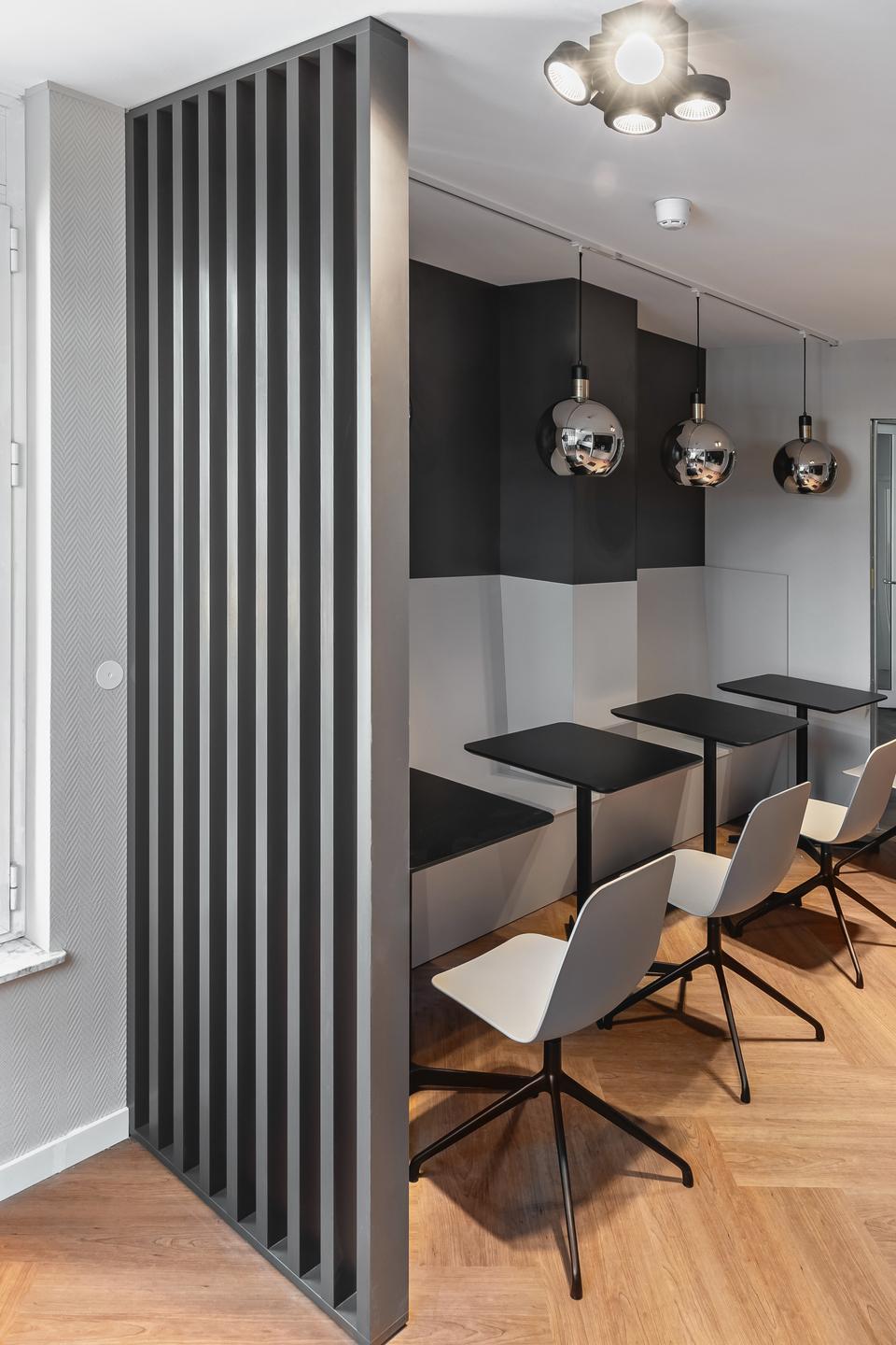 Seating niche with wall cladding and black tables Seating niche with black and grey wall panels, built-in benches, black tables, white chairs, slatted divider and three pendant lights