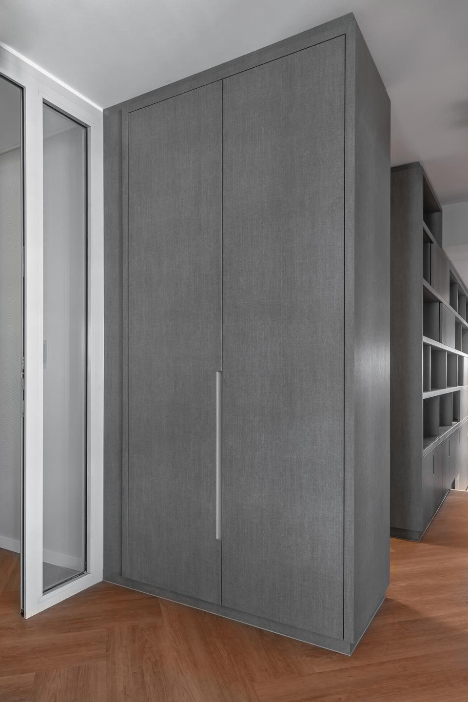 Large built-in cabinet in grey finish with recessed handle Built-in cabinet with smooth grey surface, vertical recessed handle and adjacent shelving unit on herringbone parquet floor