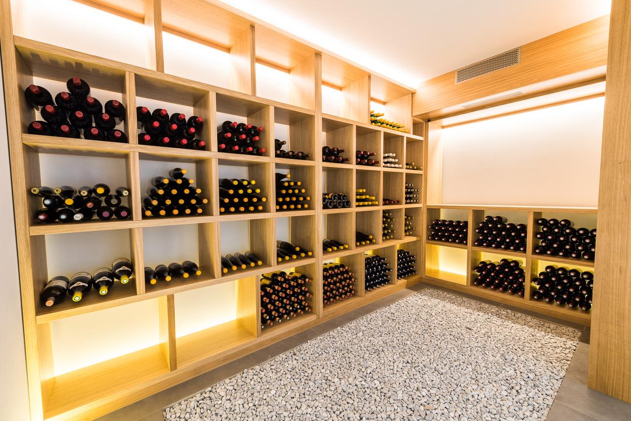 Raum mit offenen Weinregalen aus hellem Holz, sortierten Weinflaschen, integrierter Beleuchtung und Kiesboden