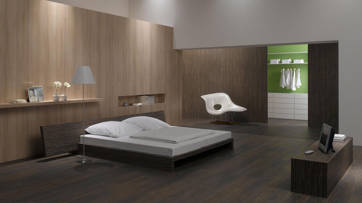 Schlafzimmerimpression mit Holzverkleidung an Wand Schlafzimmerimpression von Bett, Nachtisch und Sideboard mit Holzverkleidung an Wand und indirektert Beleuchtung