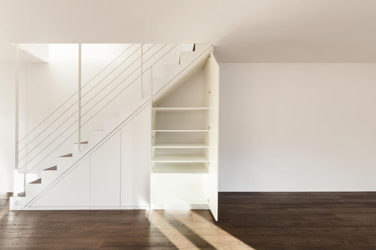 Nischenlösung für Einbauschrank unter Treppe Geräumiger Einbauschrank unter weißer Treppe mit Schubläden und Türen und offener Regalgestaltung an dunklem Parkett