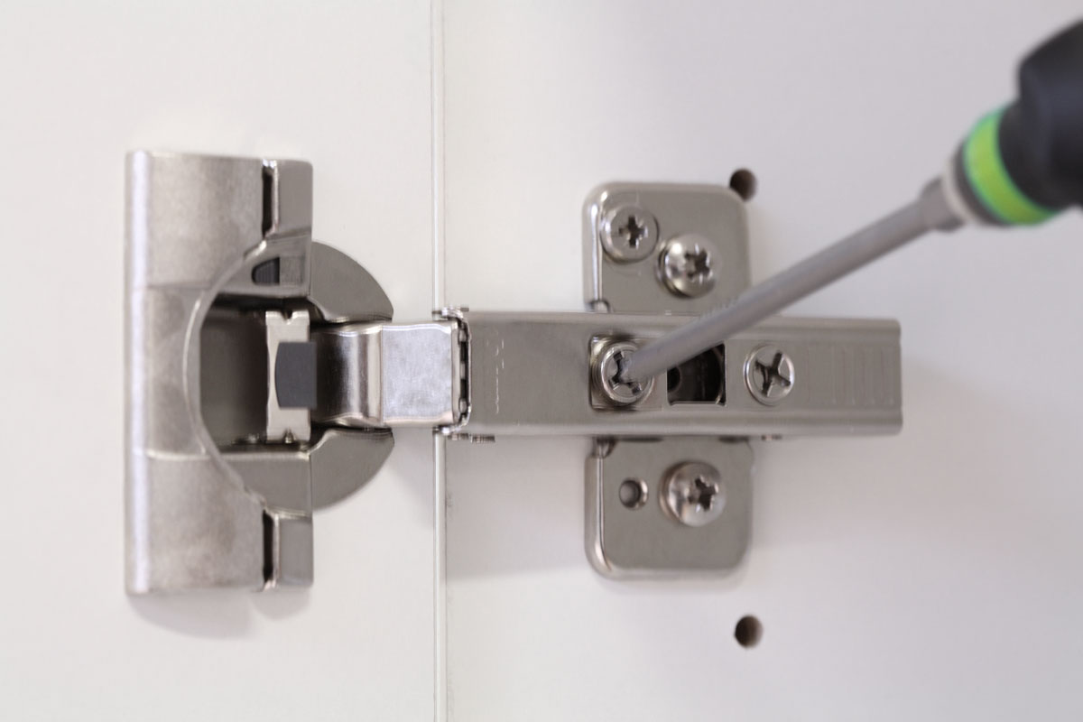 Detailaufnahme eines nachjustierbaren Türscharniers Detailaufnahme eines mit Schraubendreher nachjustierbaren Türscharniers